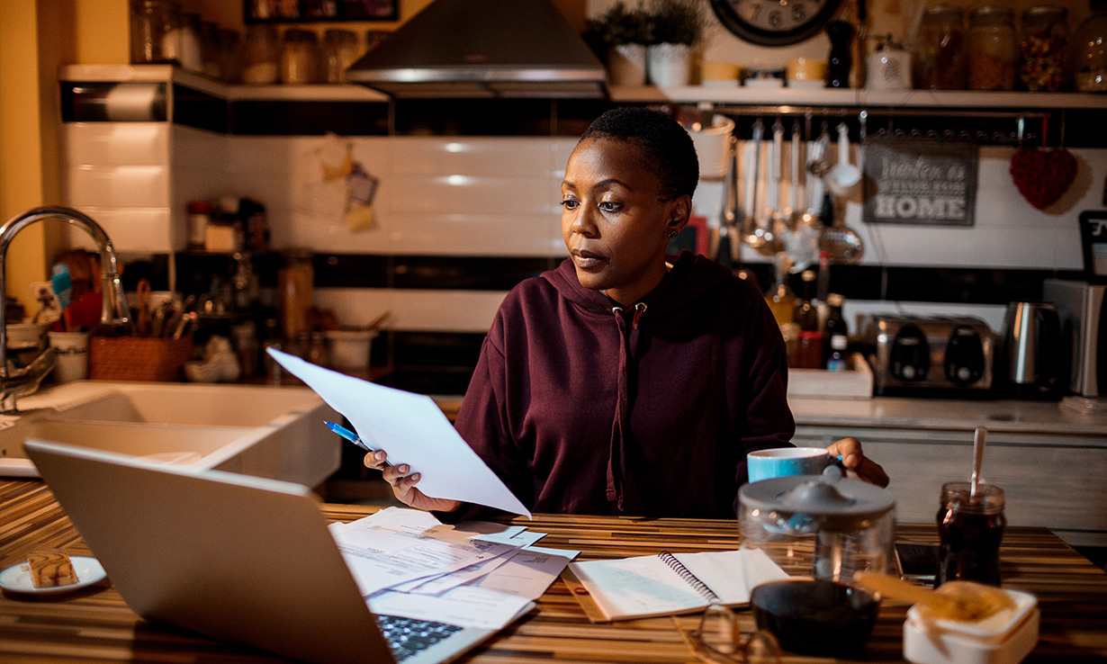 Woman sitting in a kitchen looking horrified at an energy bill
